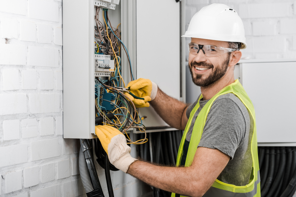 Electrician working on a a mess of wires in an electrical circuit panel - signs your home needs rewiring. 